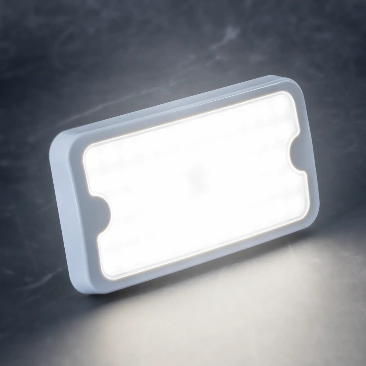 Rectangular white LED light panel glowing on a dark textured surface